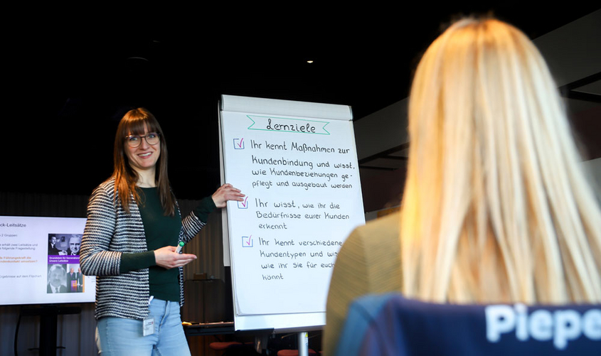 Person erklärt etwas am Flip Chart. Eine andere Person schaut zu.