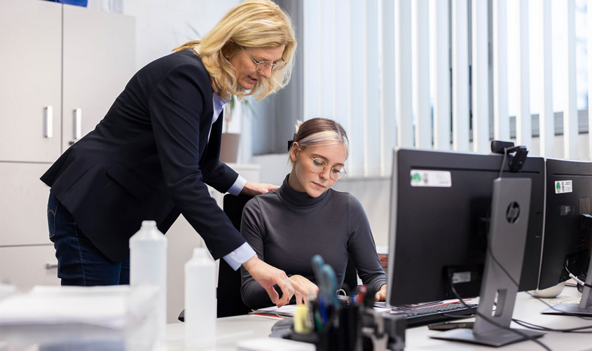 Zwei personen am Schreibtisch vor dem Computer gucken gemeinsam auf Unterlagen