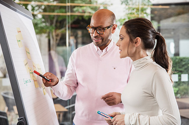 Zwei Personen unterhalten sich über Informationen auf einem Flipchart.